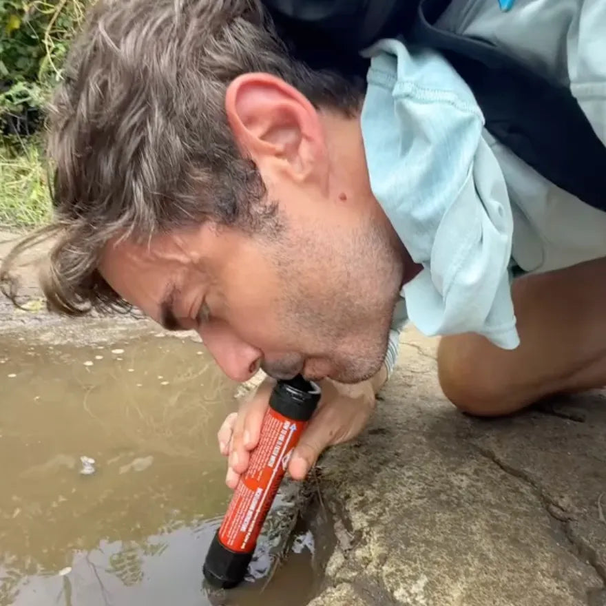 Man drinking puddle water through a filter straw